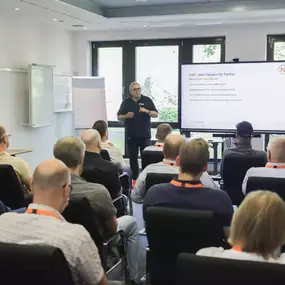 Referent hält Business-Präsentation vor Publikum im Seminarraum mit Screen