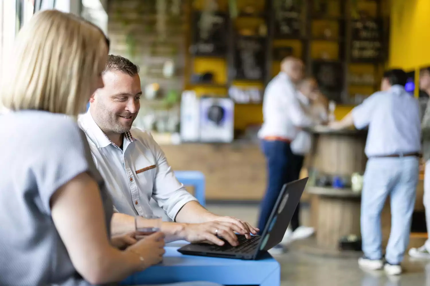 Mann arbeitet am Laptop im Coworking Space, Kollegin im Vordergrund.